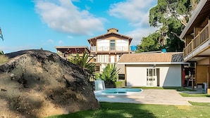 A modern house with a large rock in the foreground, a swimming pool, and a well-maintained lawn.