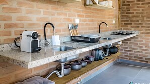 A kitchen with a brick wall, a countertop with a sink, and various kitchen utensils.