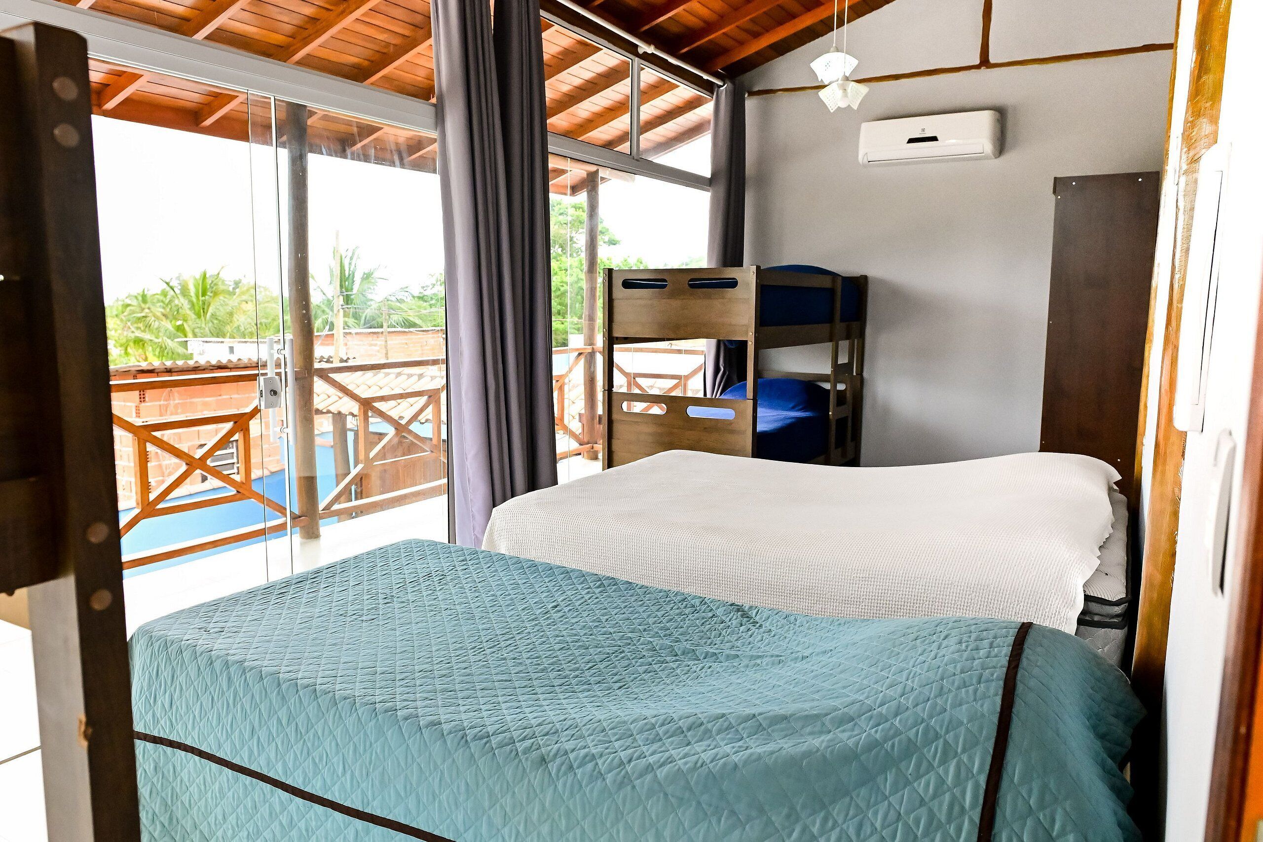 Una habitación con una litera y una cama individual, ventanas amplias y un equipo de aire acondicionado.