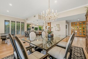 Un espace repas comprenant une table en verre, des chaises, un lustre et une vue sur l’extérieur.