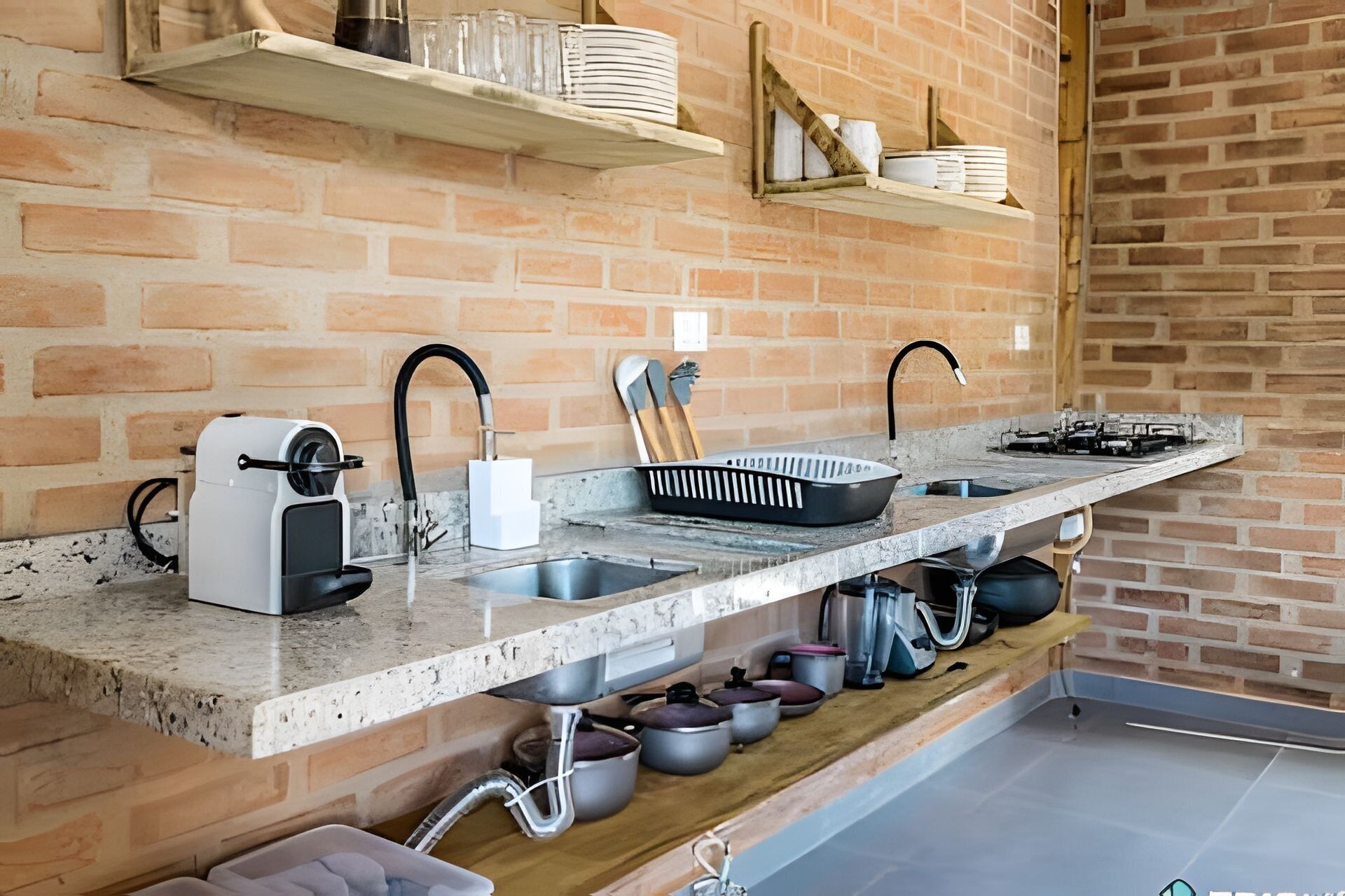 A kitchen with a brick wall, a countertop with a sink, and various kitchen utensils.