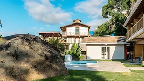 A modern house with a large rock in the foreground, a swimming pool, and a well-maintained lawn. - Recanto Feiticeira | Family suite in Feiticeira (Ilhabela)