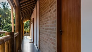 A corridor with wooden railings and a brick wall, leading to a balcony with a view of greenery. - Recanto Feiticeira | Family suite in Feiticeira (Ilhabela)