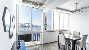 Un espace de salle à manger moderne, avec une table et des chaises, de grandes fenêtres offrant une vue sur la ville et un luminaire au plafond.