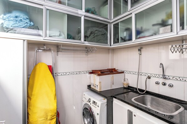 A compact kitchen with a washing machine, a sink, and a drying rack. - Botafogo: amplo com vista para o mar (Rio de Janeiro)