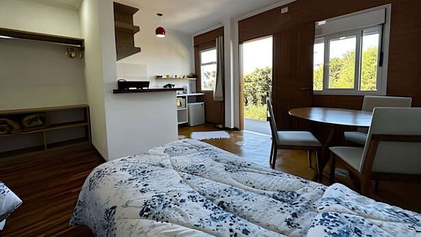 A bedroom with a bed, a desk, and a chair. There is a window with a view of trees. - Saint Louis | Studio 3 to 4 min from the center (Campos do Jordão)