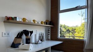 A kitchen with a window, a countertop with utensils, and shelves with kitchenware. - Saint Louis | Studio 3 to 4 min from the center (Campos do Jordão)