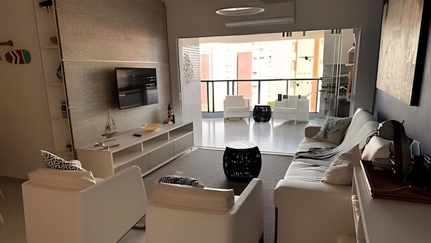 Ein modernes Wohnzimmer mit weißen Möbeln, einem an der Wand befestigten Flachbildfernseher und Blick ins Freie durch große Fenster.