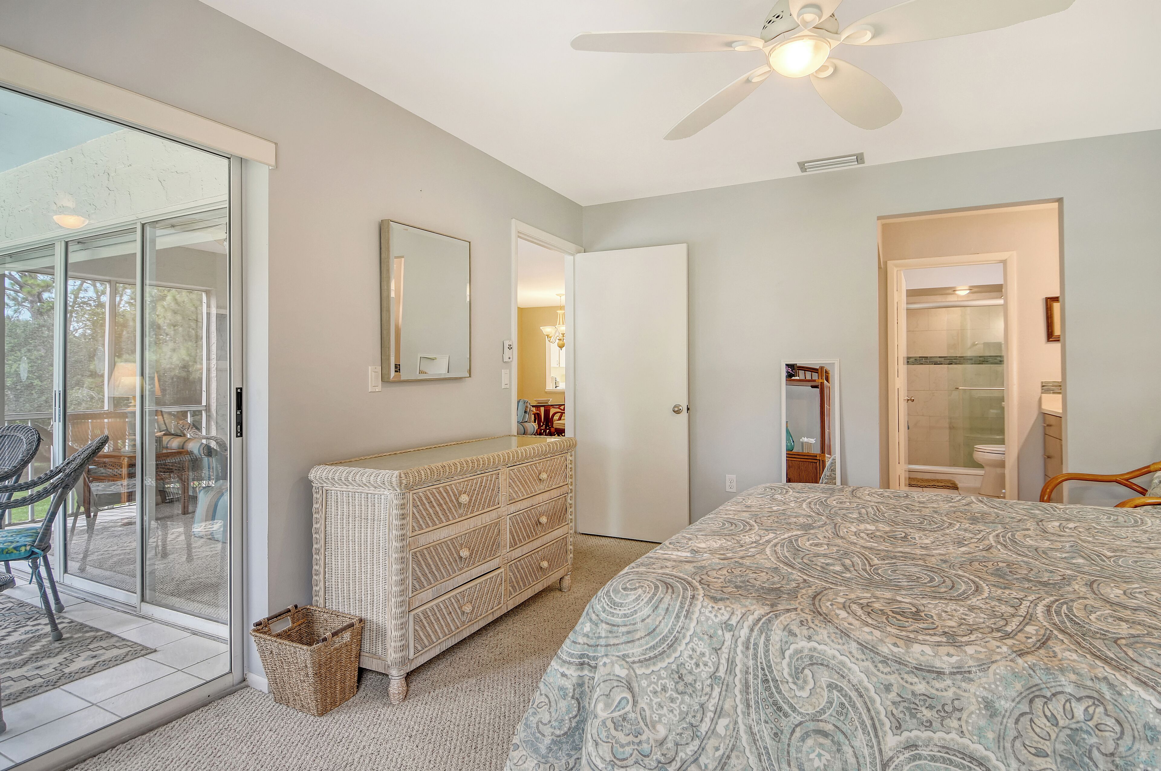 A bedroom with a large bed, a dresser, a ceiling fan, and a sliding glass door leading to a patio.