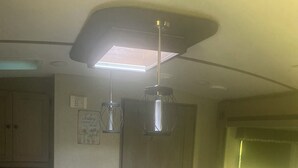 Une cuisine compacte dotée d’un îlot central, d’un four à micro-ondes, d’un évier avec un robinet moderne et de luminaires suspendus.