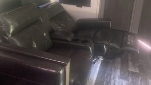 Une pièce comprenant un canapé d’angle, un téléviseur à écran plat fixé au mur et une porte en bois.