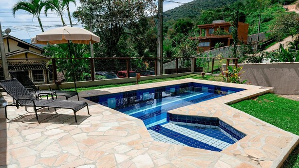 A swimming pool with stone tiles, surrounded by a wooden deck and a stone patio. - Ponta do Sol | 4 suítes, piscina e churrasqueira (Ilhabela)