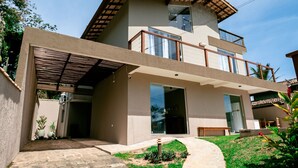 A modern two-story house with a flat roof, large windows, and a covered patio area. - Ponta do Sol | 4 suítes, piscina e churrasqueira (Ilhabela)