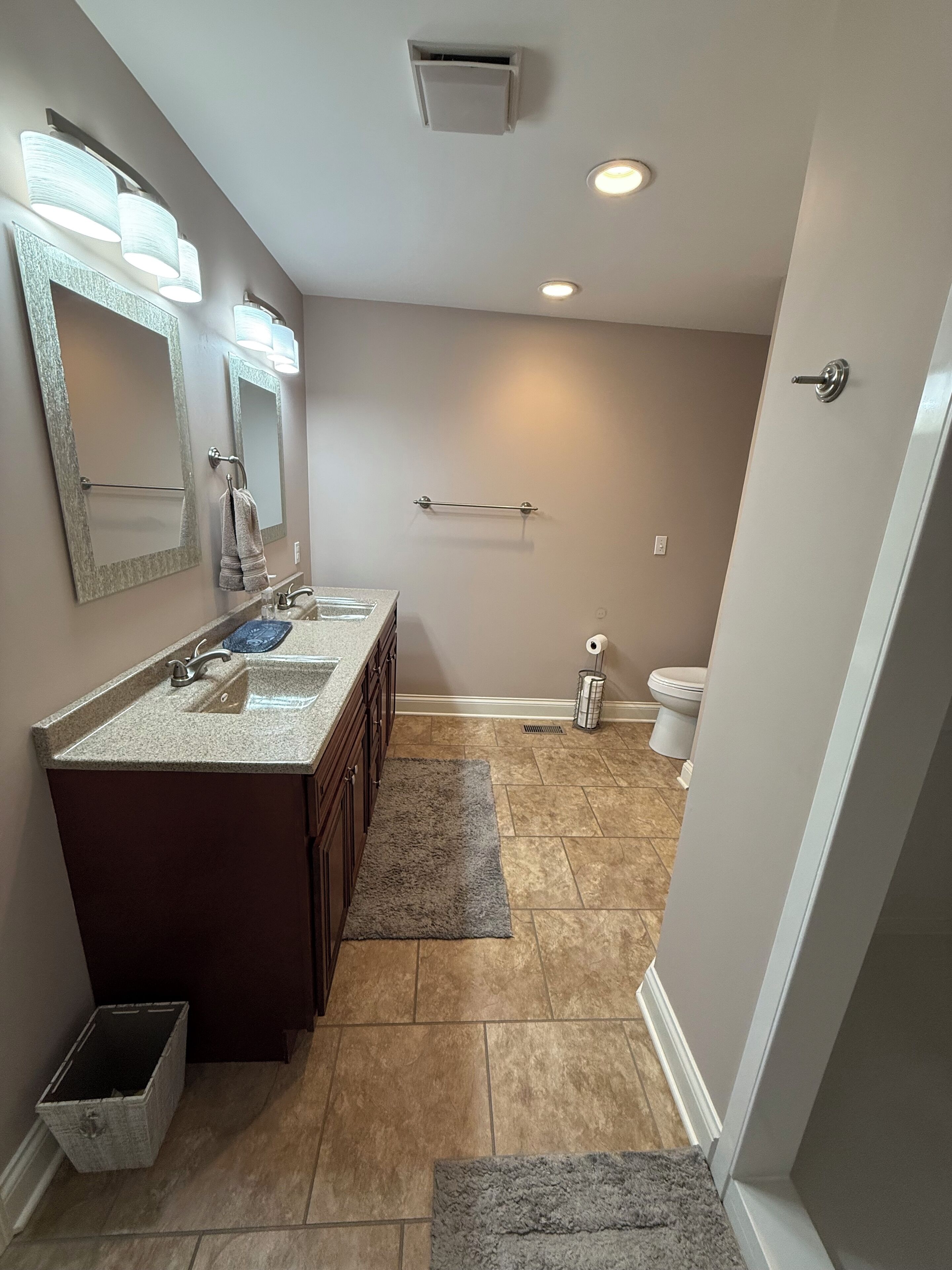 A modern bathroom with a granite sink, double vanity mirrors, a towel rack, a toilet, and a shower area.