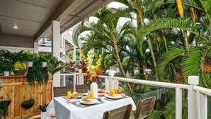 An outdoor dining area with a table set for two, surrounded by lush tropical plants and a wooden fence. - Grand Champions (Kihei)