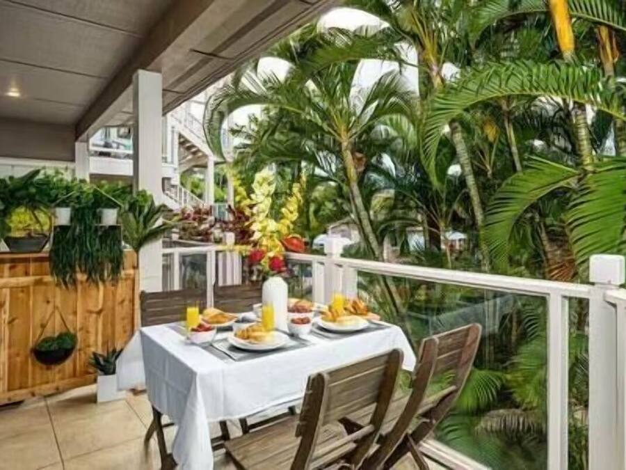 An indoor dining area with a table set for two, surrounded by lush tropical plants and a view of a staircase.