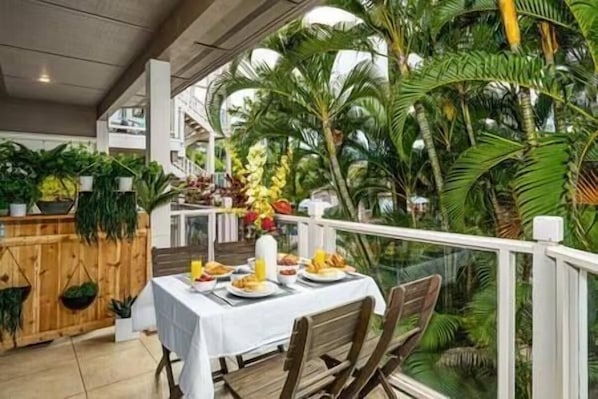 An indoor dining area with a table set for two, surrounded by lush tropical plants and a view of a staircase. - Grand Champions (Kihei)