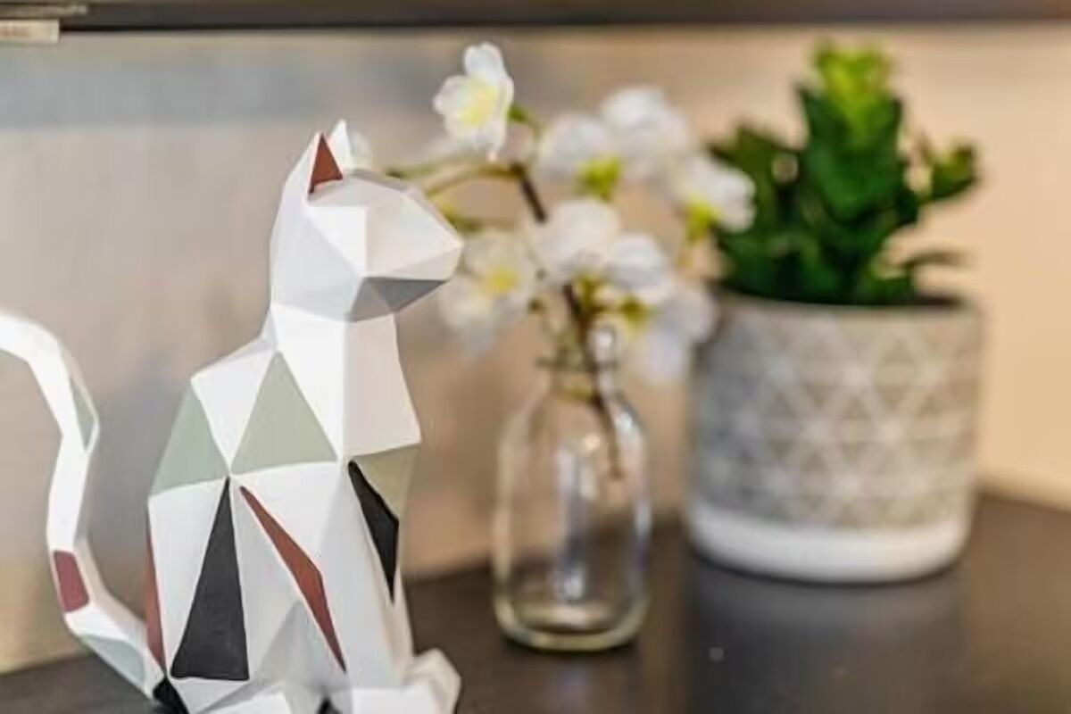 A geometric cat figurine on a table with a potted plant in the background.