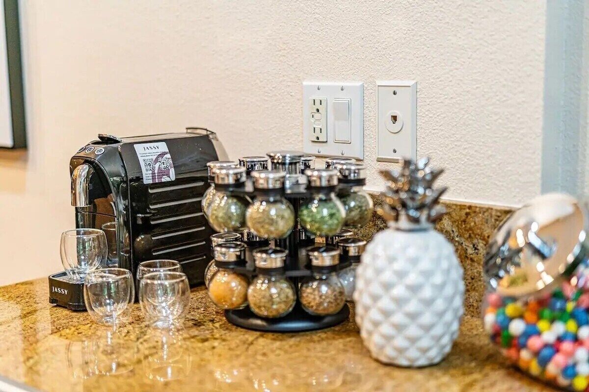 A kitchen counter with a coffee machine, salt and pepper shakers, a pineapple-shaped container, and a jar of colorful candies.