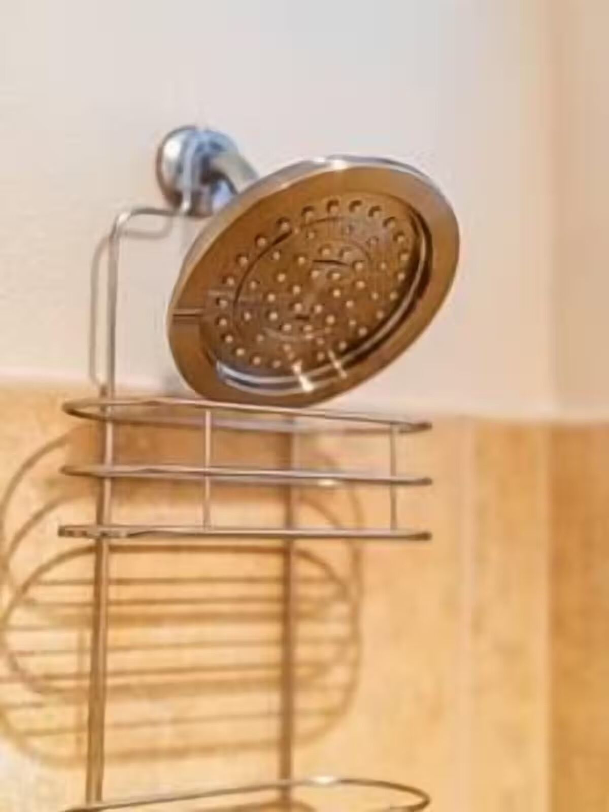 Une salle de bain avec une pomme de douche fixée au mur, un étagère métallique à plusieurs niveaux et un mur recouvert de carreaux.