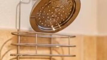 Une salle de bain avec une pomme de douche fixée au mur, un étagère métallique à plusieurs niveaux et un mur recouvert de carreaux.