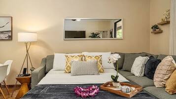 Una habitación de hotel con una cama, una mesita de noche con lámpara, un espejo, un sofá y una planta pequeña.