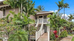A two-story building with a balcony on the upper floor, surrounded by lush tropical vegetation. - Grand Champions (Kihei)