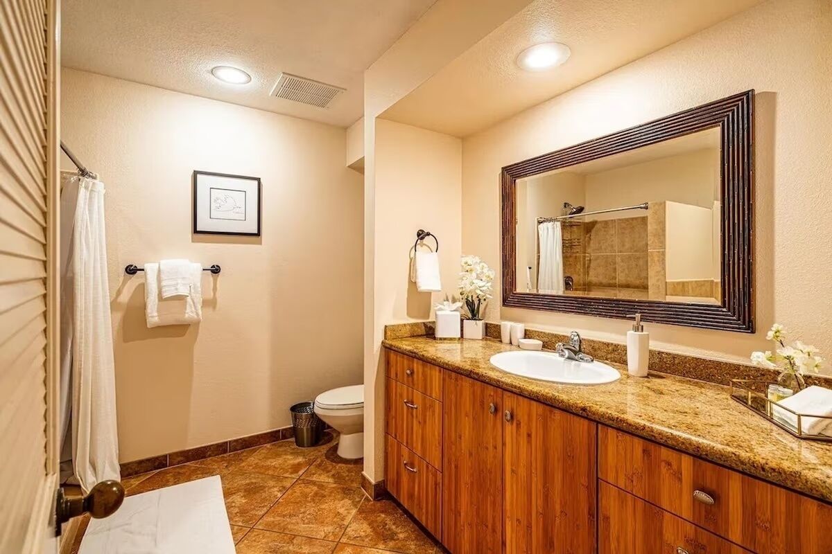 A bathroom with a wooden vanity, a large mirror, and a toilet.