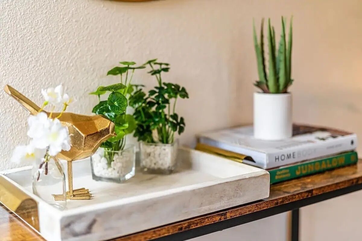 Une étagère en marbre ornée d’une sculpture d’oiseau en or, de petites plantes en pot et de livres.