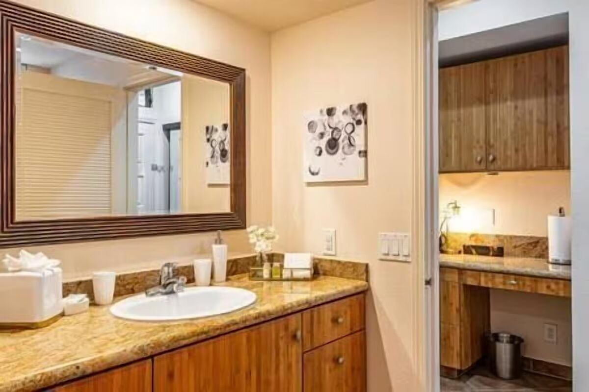 A bathroom with a large mirror, a sink, and wooden cabinets.
