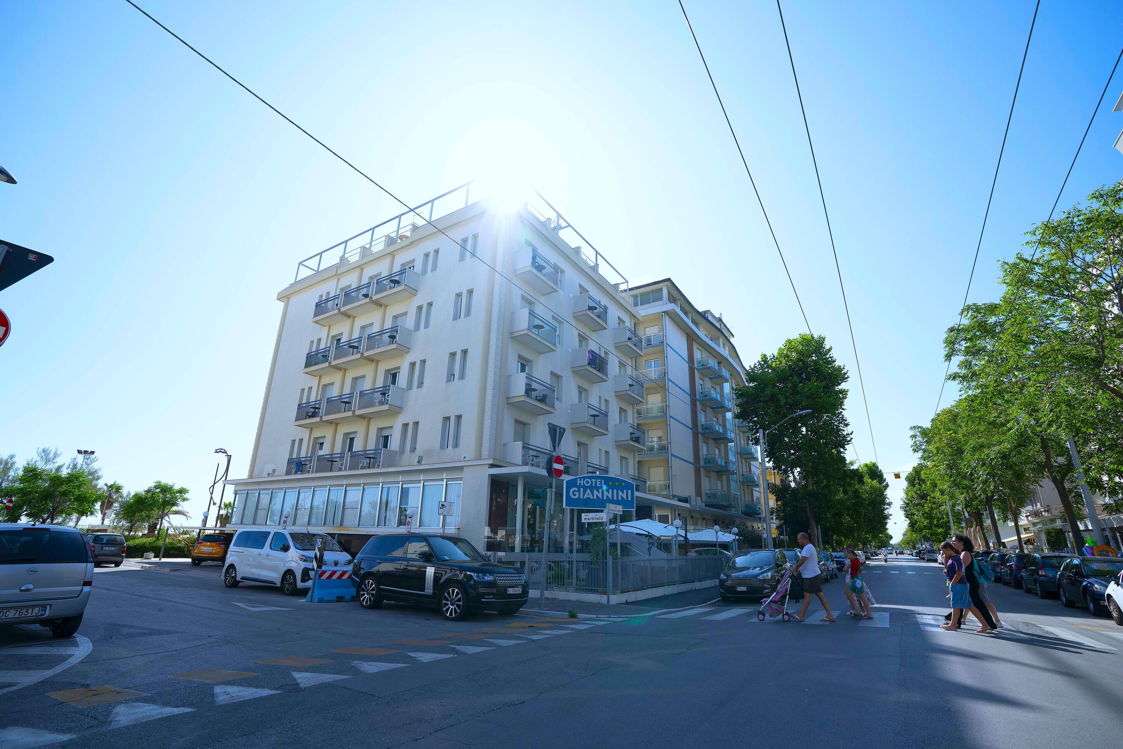 Et hotel med flere etager, altaner, en klar himmel og parkerede biler.