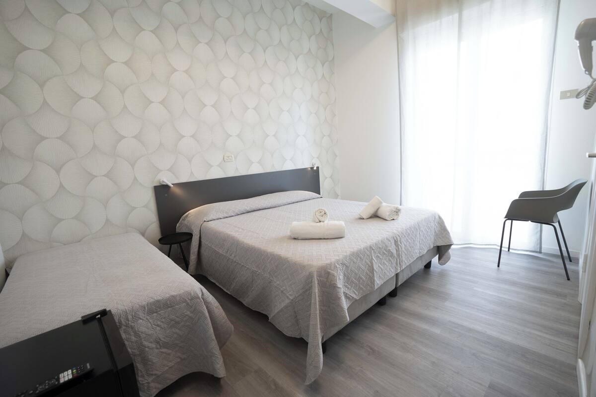 A modern hotel room with two beds, a small table, and a chair.