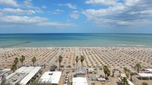 Une plage avec de nombreux parasols et des chaises longues, une jetée en arrière-plan et un ciel dégagé.
