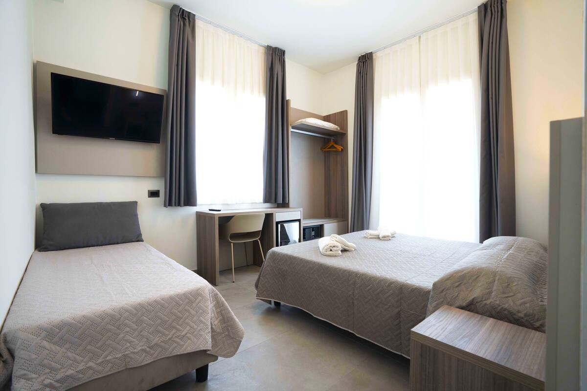 A hotel room with two beds, a desk, a chair, a TV, and a wardrobe.