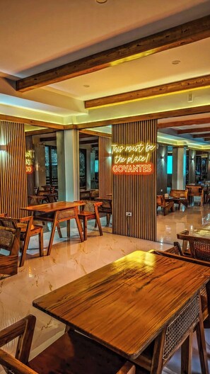A restaurant interior with wooden furniture, a neon sign, and a view of the outside. - The Tree House @Govantes Guesthouse (Vigan City)