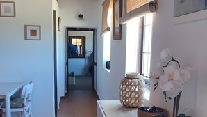 Un pasillo con techo de madera, un mostrador blanco con adornos y un comedor con mesa y sillas.