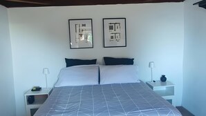 Un dormitorio con techo de madera, una cama con colcha de estampado geométrico, dos cuadros en la pared y una mesita de noche con lámpara.