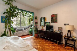 Una habitación con una hamaca, una cama, un televisor, un escritorio y varias decoraciones en las paredes.