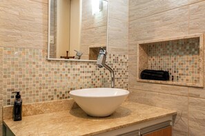 Un baño con lavamanos blanco, un espejo, toallero y dispensador de jabón.