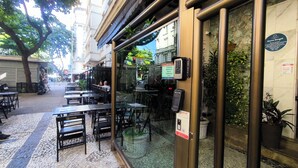 An outdoor café with tables and chairs, a glass door entrance, and a signboard. - Copacabana 2 quartos na quadra da praia. (Rio de Janeiro)