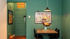 A dining area with a table, chairs, a vase of flowers, a hanging light, and a door with a green door. - Copacabana 2 quartos na quadra da praia. (Rio de Janeiro)