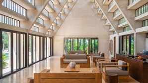 A spacious lobby with a high ceiling, large windows, and a central seating area with sofas and wooden tables. - Peregrina Tulum 302B 1BR Condo (Tulum)