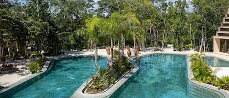 Un área de piscina con dos piscinas separadas, rodeada de exuberante vegetación y una estructura de edificio moderna.