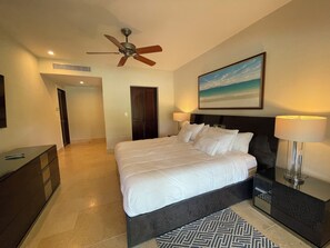 Ein Hotelzimmer mit einem großen Bett, einem Deckenventilator, einem Strandbild und einem Nachttisch mit Lampe.