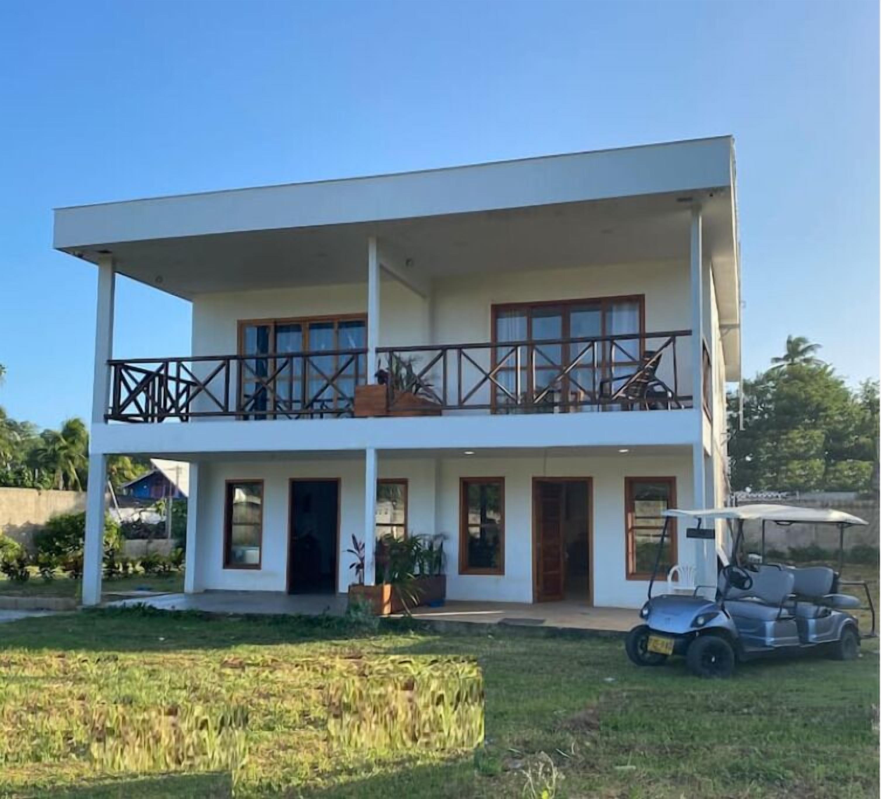 A two-story building with a balcony, a golf cart, and a lawn in front.