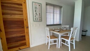 A dining area with a wooden door, a window with blinds, and a table with white chairs.