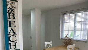 A dining area with a wooden table and chairs, a window with blinds, and a wall-mounted sign.