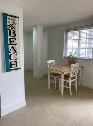 A dining area with a wooden table and chairs, a window with blinds, and a wall-mounted sign.