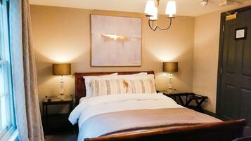 A neatly made bed with a wooden headboard, two bedside lamps, a wall-mounted artwork, and a dark door.
