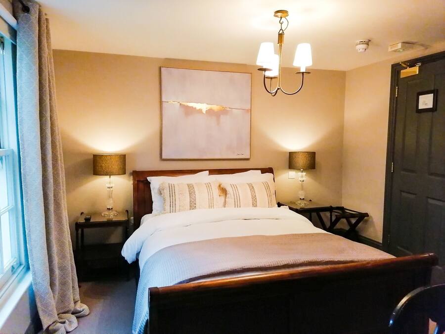 A neatly made bed with a wooden headboard, two bedside lamps, a wall-mounted artwork, and a dark door.
